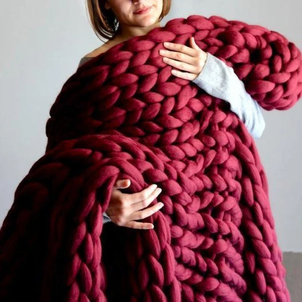 Frau mit großer, roter, grob gestrickter Decke aus Wolle, gemütlich, warm, handgefertigt.